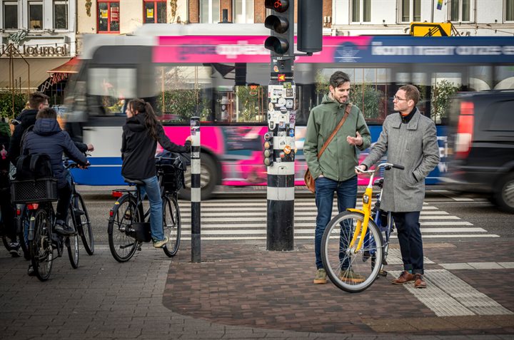 Xavier en Willie in gesprek bij een stoplicht, op de achtergrond fietsers en verkeer