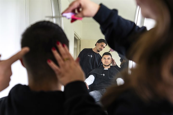 Een jongere in kappersstoel kijkt toe hoe zijn haar geknipt wordt